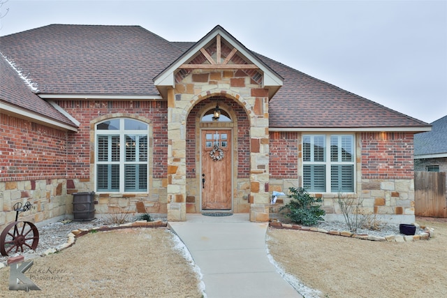 view of front facade with stone siding, brick siding, and roof with shingles