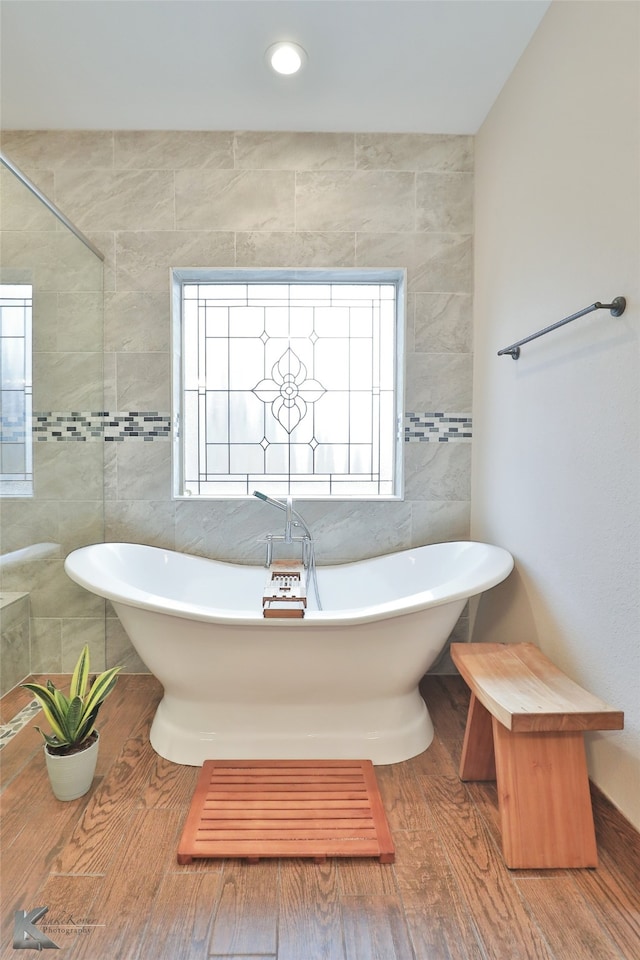 full bathroom featuring a freestanding bath, wood finished floors, and tile walls