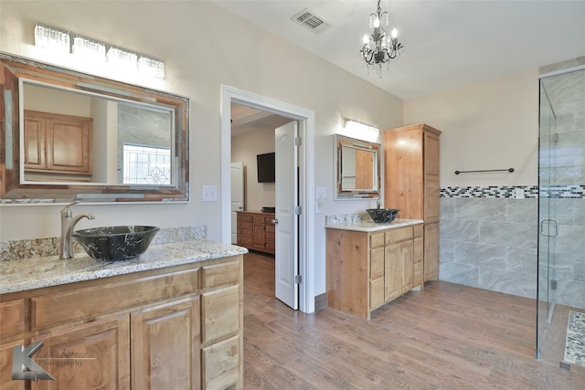 bathroom featuring wood finished floors, two vanities, a sink, visible vents, and a shower stall