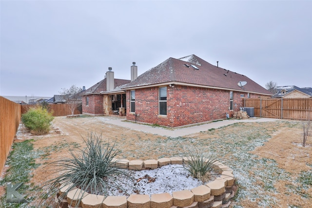 rear view of property featuring a fenced backyard, a chimney, cooling unit, and brick siding