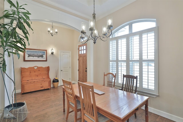 dining room with baseboards, arched walkways, ornamental molding, wood finished floors, and an inviting chandelier