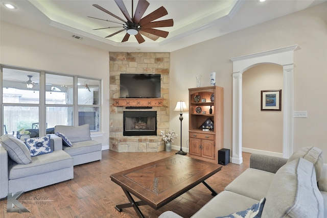 living room with a tray ceiling, wood finished floors, a ceiling fan, and ornate columns