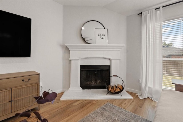 living room featuring vaulted ceiling, baseboards, a fireplace with raised hearth, and wood finished floors