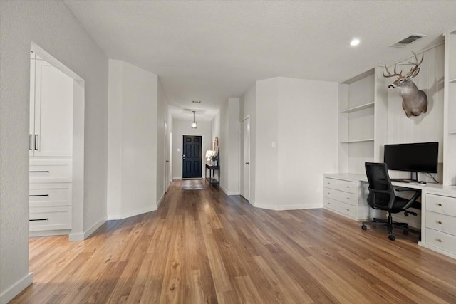 unfurnished office with light wood finished floors, visible vents, baseboards, and a textured ceiling