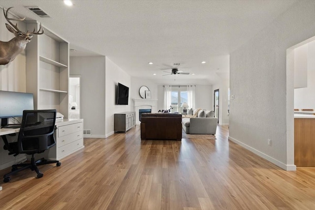 living area featuring built in shelves, a fireplace, visible vents, light wood-style floors, and baseboards