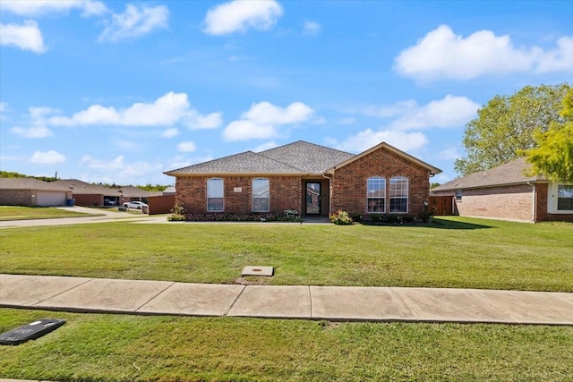 ranch-style home featuring a shingled roof, a front yard, brick siding, and fence