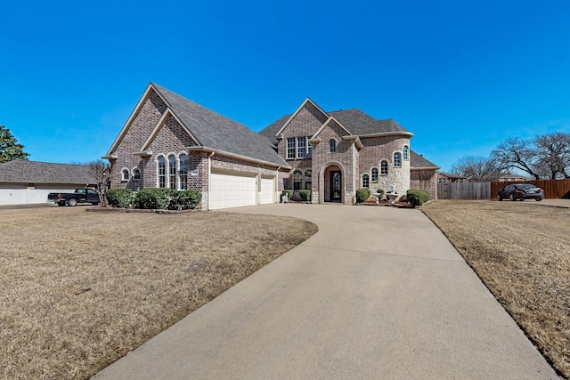 french provincial home featuring fence, a front lawn, concrete driveway, and brick siding