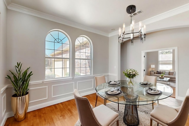 dining room featuring a decorative wall, visible vents, light wood-style floors, ornamental molding, and an inviting chandelier