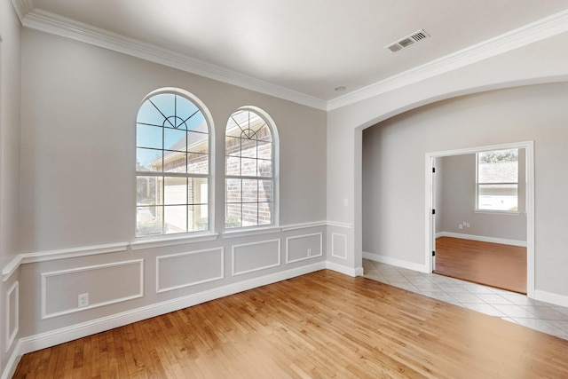 unfurnished room with arched walkways, crown molding, light tile patterned floors, visible vents, and a decorative wall