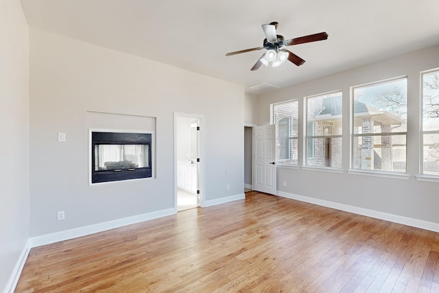 unfurnished living room with light wood-type flooring, a multi sided fireplace, ceiling fan, and baseboards