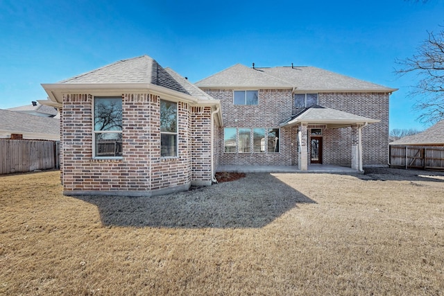 rear view of property with a shingled roof, brick siding, a yard, and fence