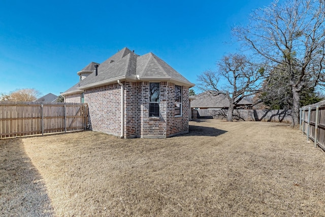 rear view of house featuring a yard, a fenced backyard, a shingled roof, and brick siding