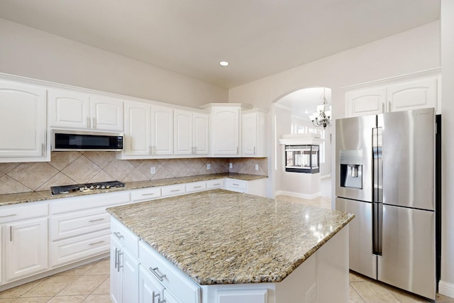 kitchen with a center island, white cabinetry, appliances with stainless steel finishes, backsplash, and light stone countertops