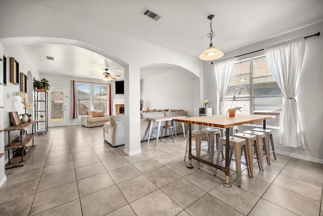 dining room with ceiling fan, a fireplace, visible vents, and light tile patterned flooring