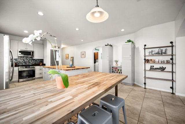 kitchen with arched walkways, stainless steel appliances, butcher block countertops, decorative backsplash, and a center island