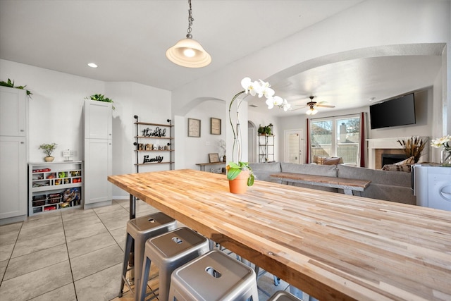 dining room featuring arched walkways, a fireplace, recessed lighting, light tile patterned flooring, and ceiling fan