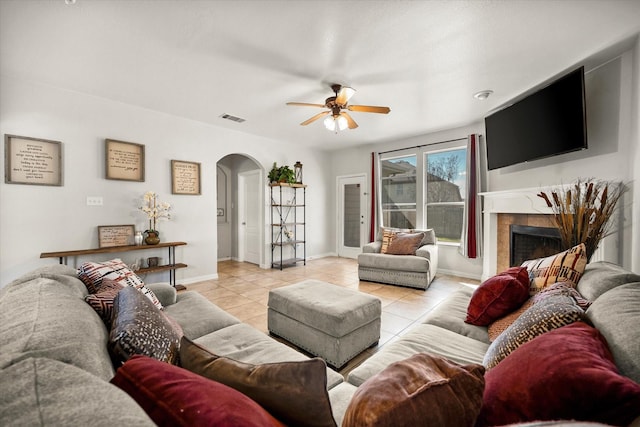 living room featuring arched walkways, light tile patterned floors, a high end fireplace, visible vents, and baseboards