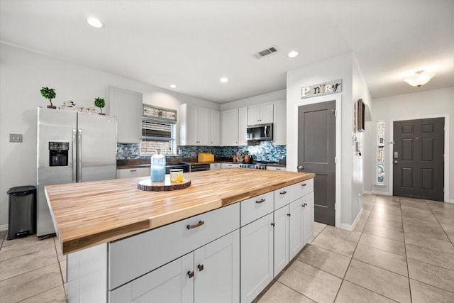 kitchen featuring light tile patterned floors, butcher block counters, visible vents, appliances with stainless steel finishes, and tasteful backsplash