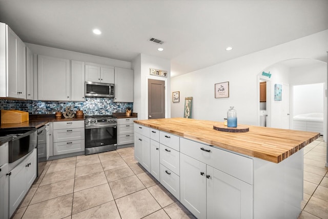 kitchen with arched walkways, light tile patterned floors, stainless steel appliances, wood counters, and decorative backsplash