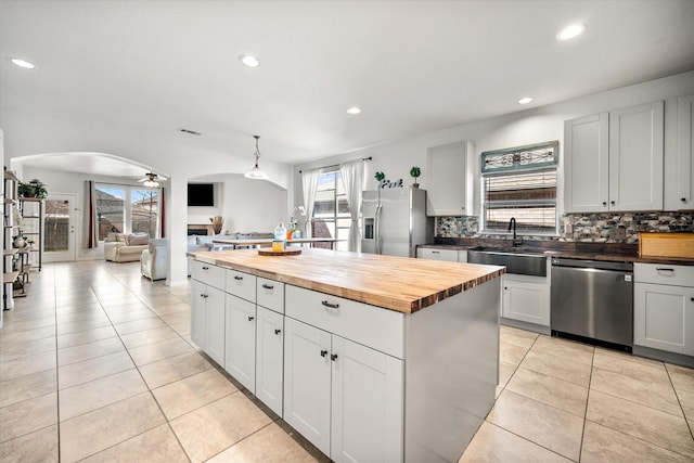 kitchen featuring arched walkways, tasteful backsplash, wooden counters, appliances with stainless steel finishes, and a sink