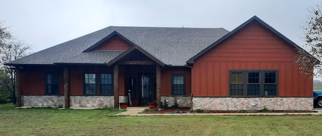 view of front of house featuring stone siding, a shingled roof, a front lawn, and board and batten siding