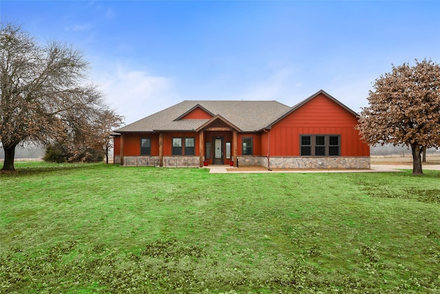 view of front of house featuring board and batten siding, a front yard, stone siding, and a shingled roof