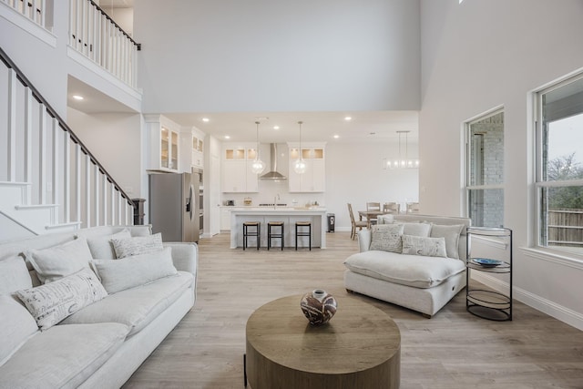 living area with baseboards, a high ceiling, stairs, and light wood-style floors