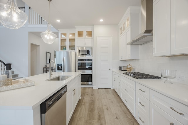 kitchen featuring wall chimney exhaust hood, light wood-style flooring, a sink, stainless steel appliances, and backsplash