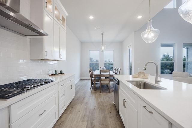 kitchen featuring appliances with stainless steel finishes, light countertops, a sink, and wall chimney exhaust hood