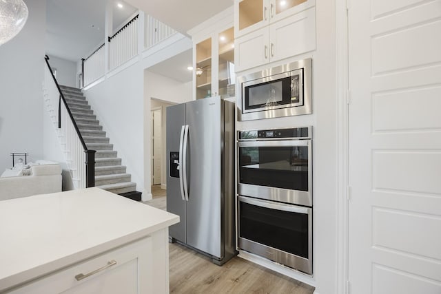 kitchen featuring light wood-style flooring, stainless steel appliances, white cabinetry, light countertops, and glass insert cabinets