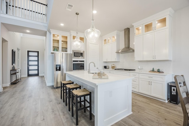 kitchen with a breakfast bar area, appliances with stainless steel finishes, light wood-style floors, a sink, and wall chimney range hood