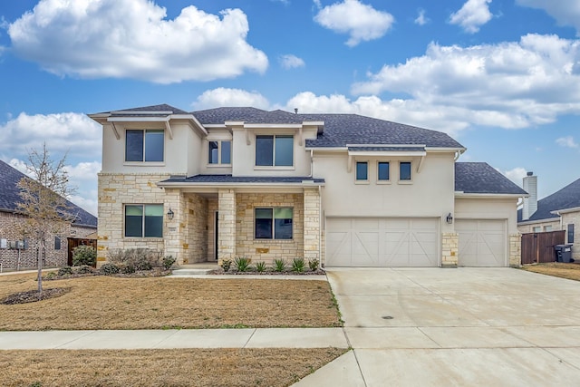 prairie-style house featuring a shingled roof, concrete driveway, stone siding, fence, and stucco siding