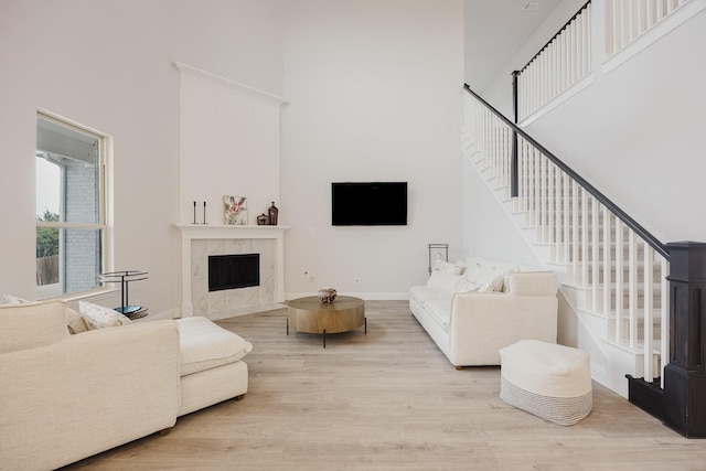 living room with a high ceiling, wood finished floors, a high end fireplace, baseboards, and stairway