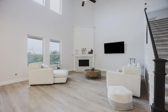 living area with baseboards, ceiling fan, a premium fireplace, stairway, and light wood-type flooring