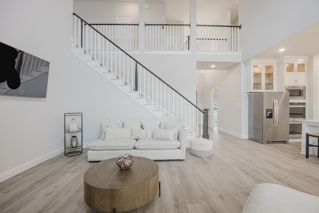 living area with stairs, light wood-type flooring, a towering ceiling, and baseboards