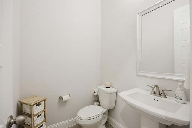 half bath featuring toilet, baseboards, and a sink