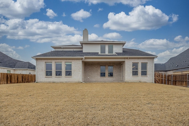 back of property featuring a fenced backyard, brick siding, a shingled roof, a lawn, and a chimney