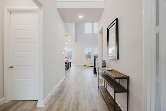 corridor featuring a high ceiling, baseboards, and light wood finished floors