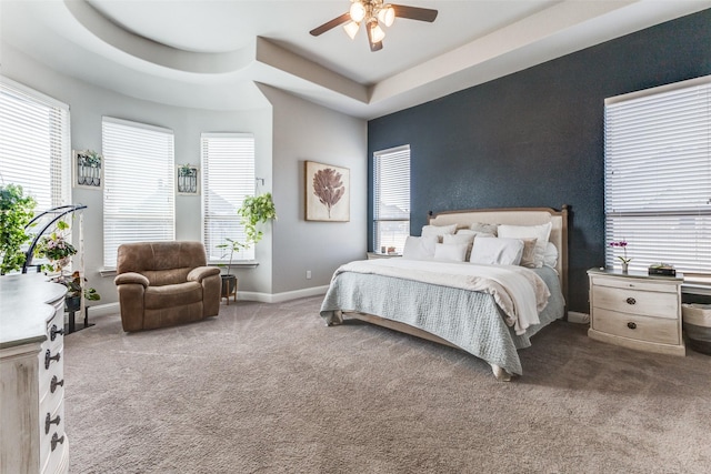 bedroom featuring carpet floors, a tray ceiling, baseboards, and a ceiling fan