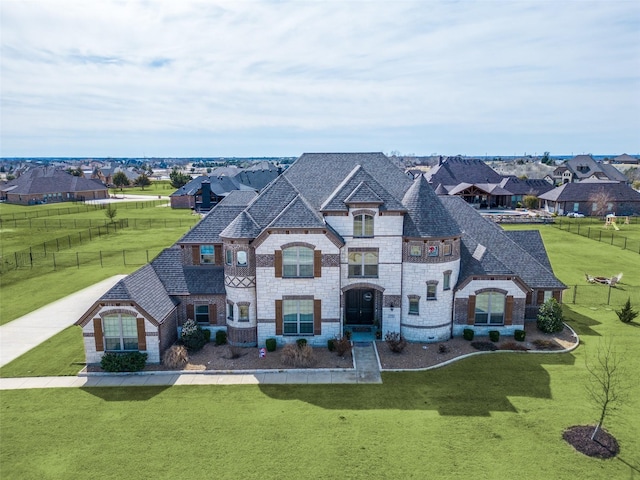 french country style house featuring brick siding, a front yard, fence, and a shingled roof