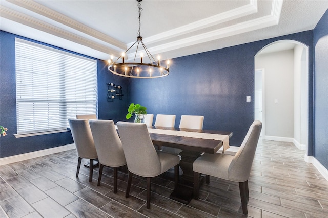 dining space featuring wood tiled floor, a tray ceiling, arched walkways, and baseboards