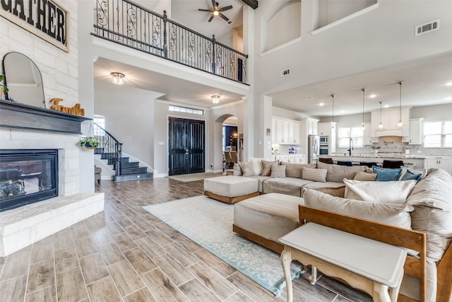 living room with arched walkways, visible vents, stairway, wood tiled floor, and a stone fireplace