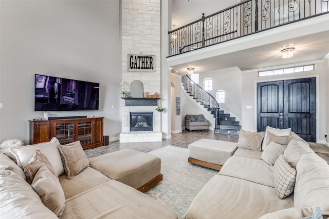 living room featuring a stone fireplace, stairway, a towering ceiling, and baseboards