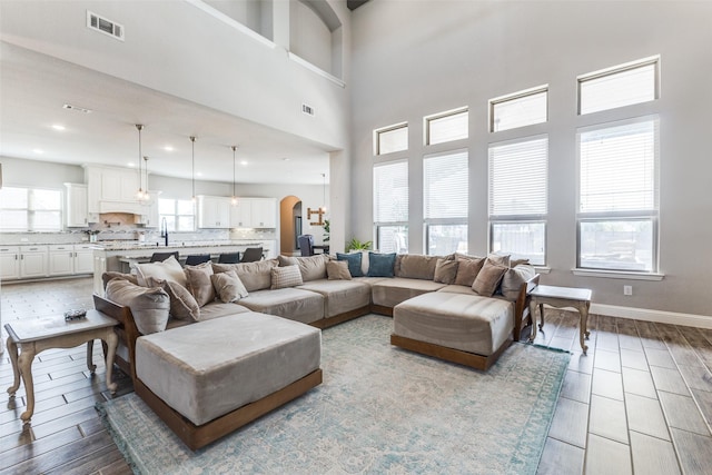 living room with visible vents, arched walkways, baseboards, a towering ceiling, and wood finished floors