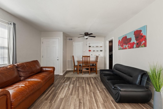 living area featuring baseboards, visible vents, ceiling fan, and wood finished floors