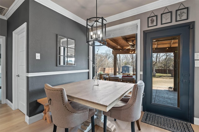 dining space with a textured wall, crown molding, baseboards, light wood-type flooring, and an inviting chandelier