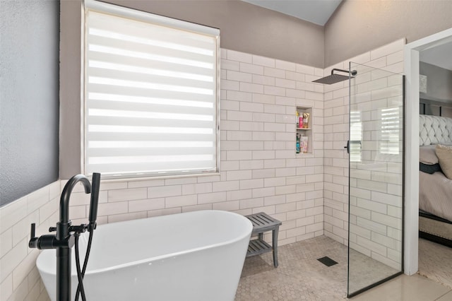 ensuite bathroom with tile walls, a textured wall, ensuite bath, a walk in shower, and a freestanding tub