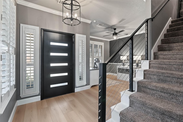 foyer featuring visible vents, ceiling fan, ornamental molding, wood finished floors, and stairs