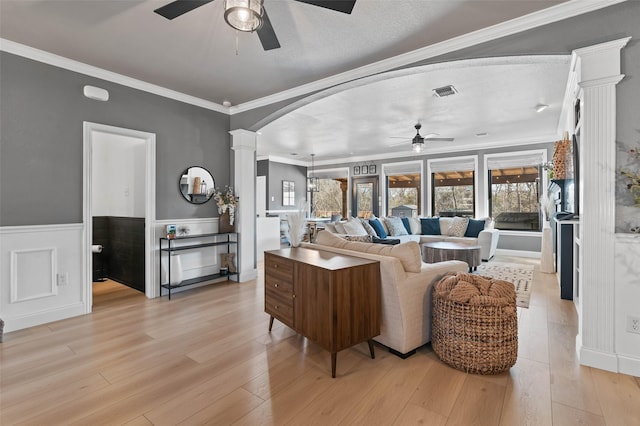 living area with light wood finished floors, decorative columns, arched walkways, and a wainscoted wall