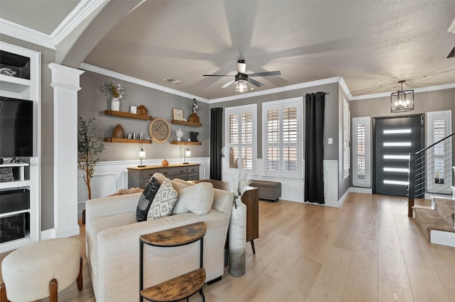 living area featuring decorative columns, arched walkways, a wainscoted wall, light wood-style flooring, and ornamental molding